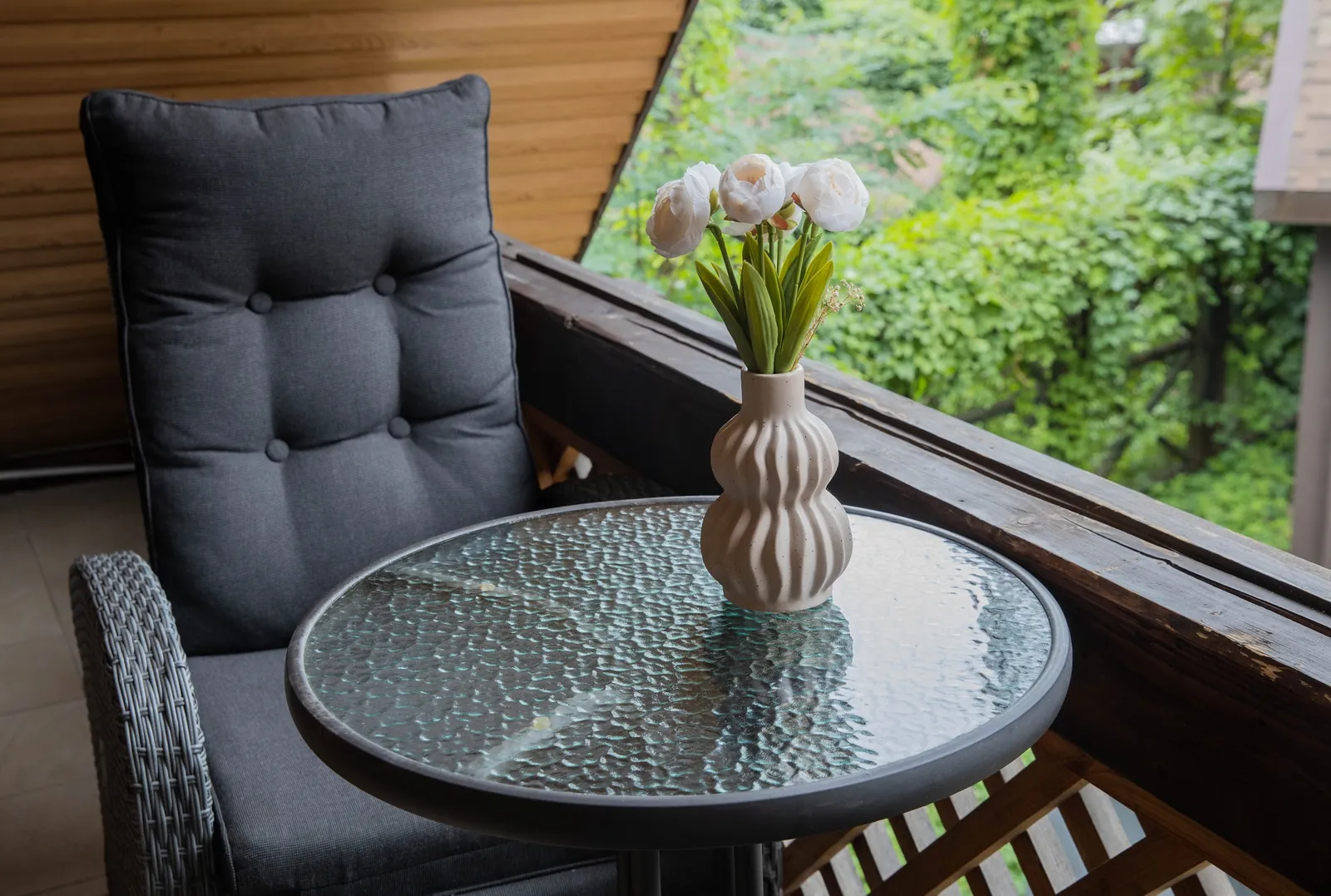 An armchair and a table on a cottage balcony overlooking the greenery